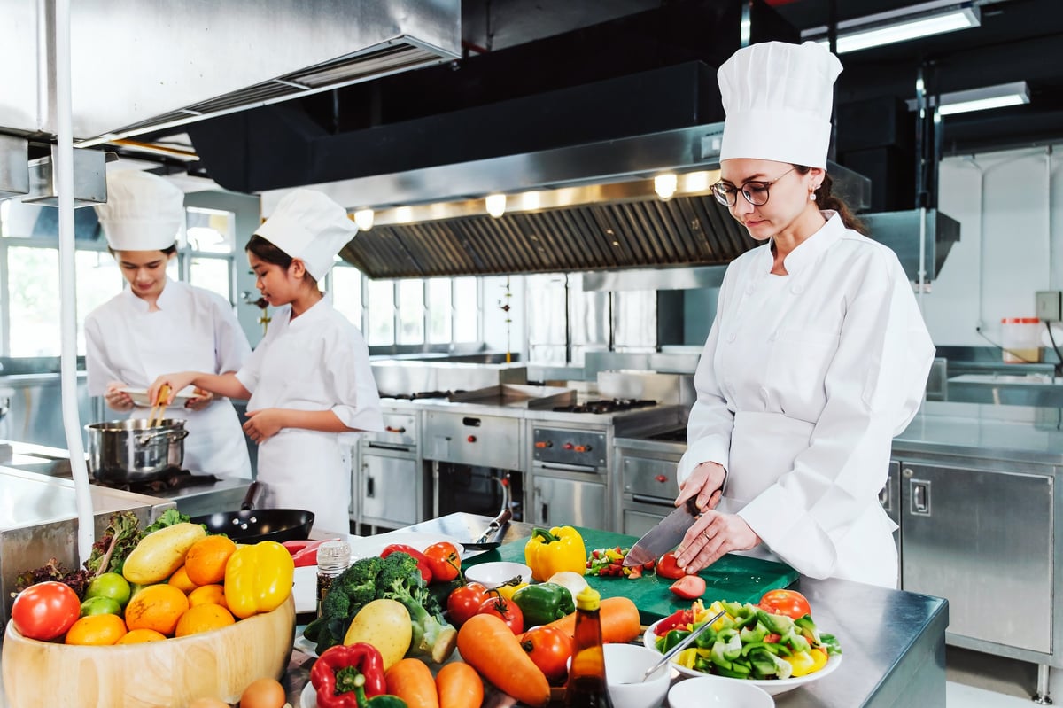 Chef slicing fresh vegetables on a cutting board in a professional kitchen